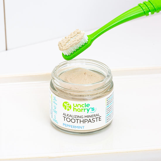 Jar of Uncle Harry's Peppermint Toothpaste with a green toothbrush scooping out some paste.