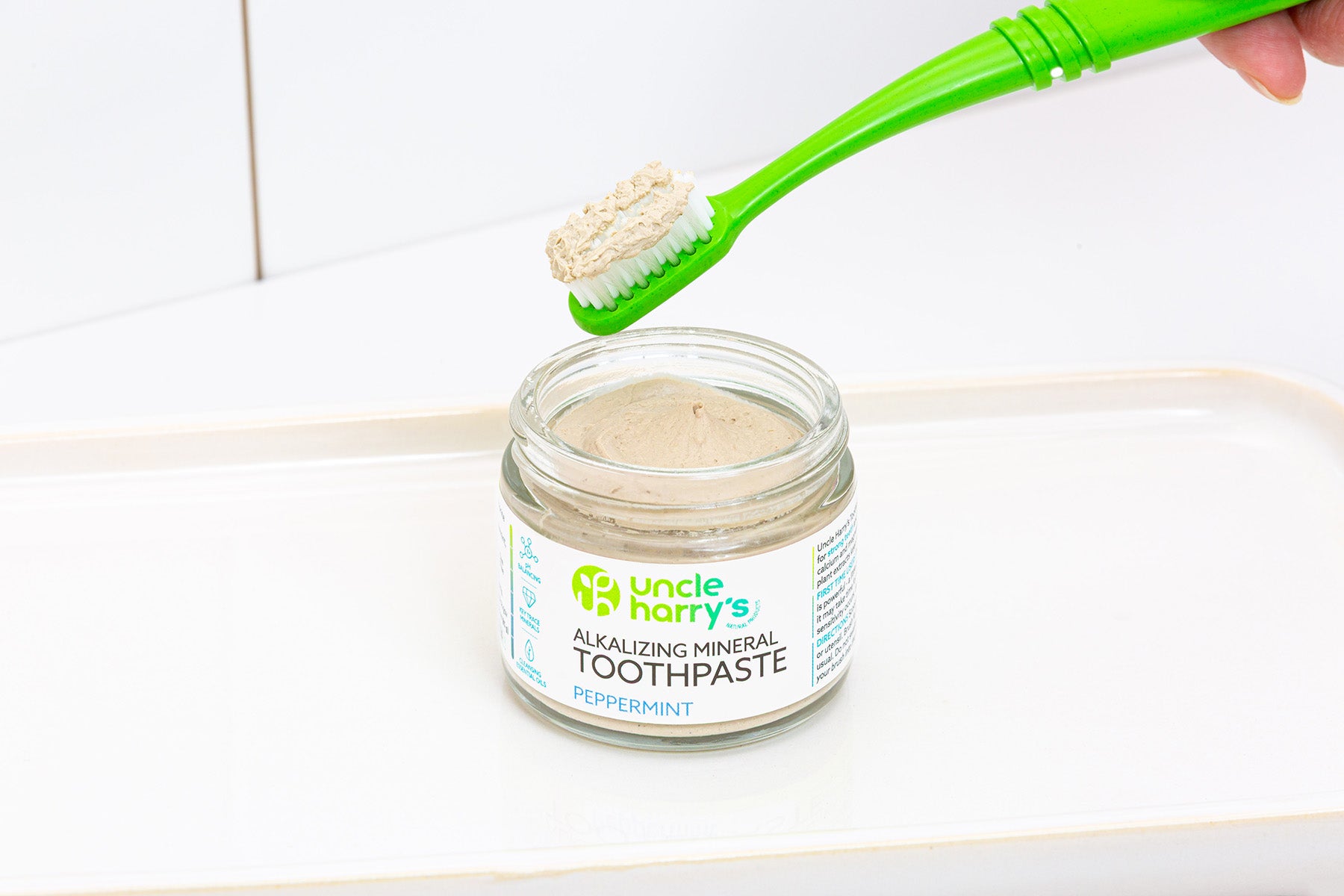 Jar of Uncle Harry's Peppermint Toothpaste with a green toothbrush scooping out some paste.