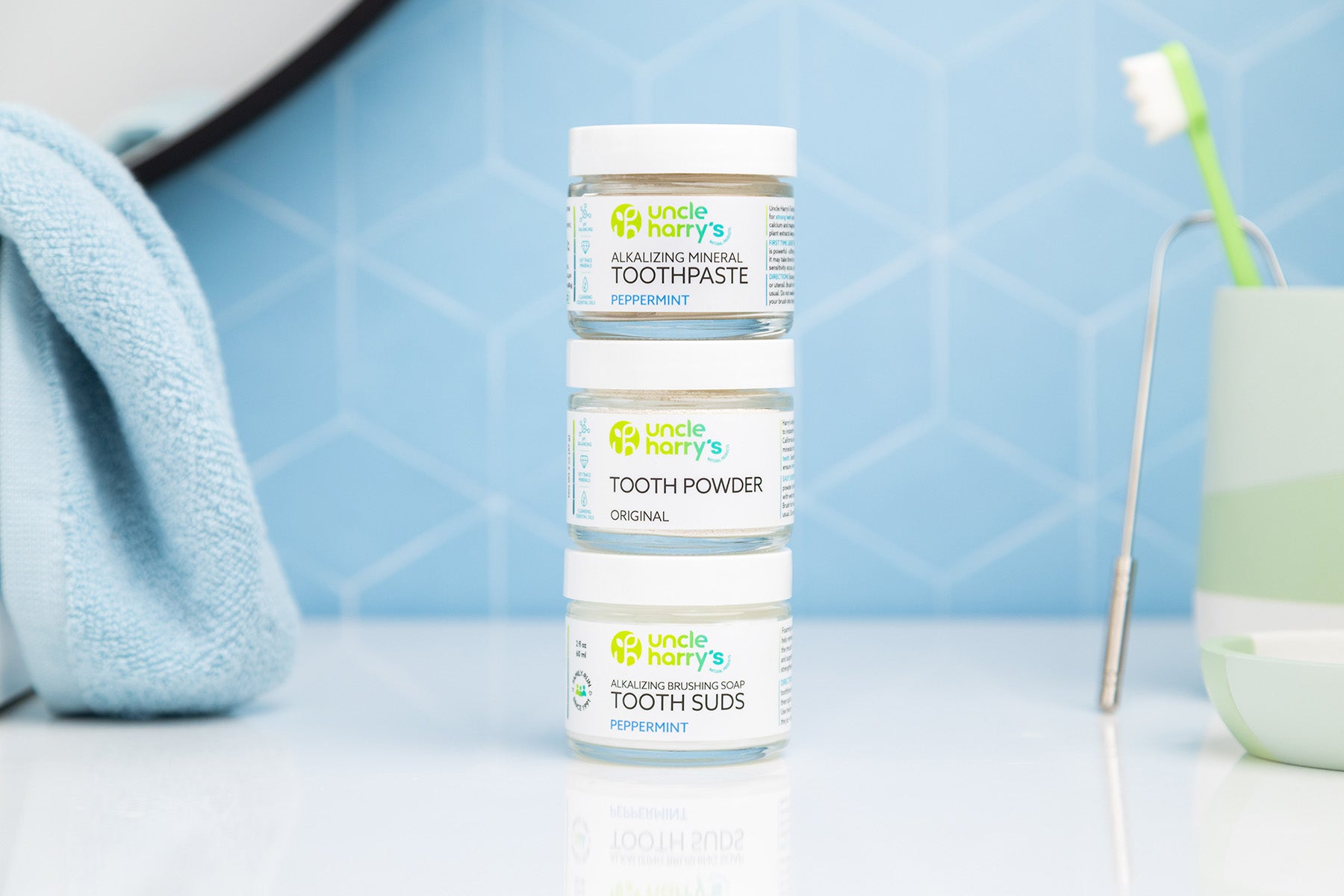 Bottles of Uncle Harry's Toothpaste, Tooth Powder, Tooth Suds on a bathroom counter with a toothbrush and glass in the background.