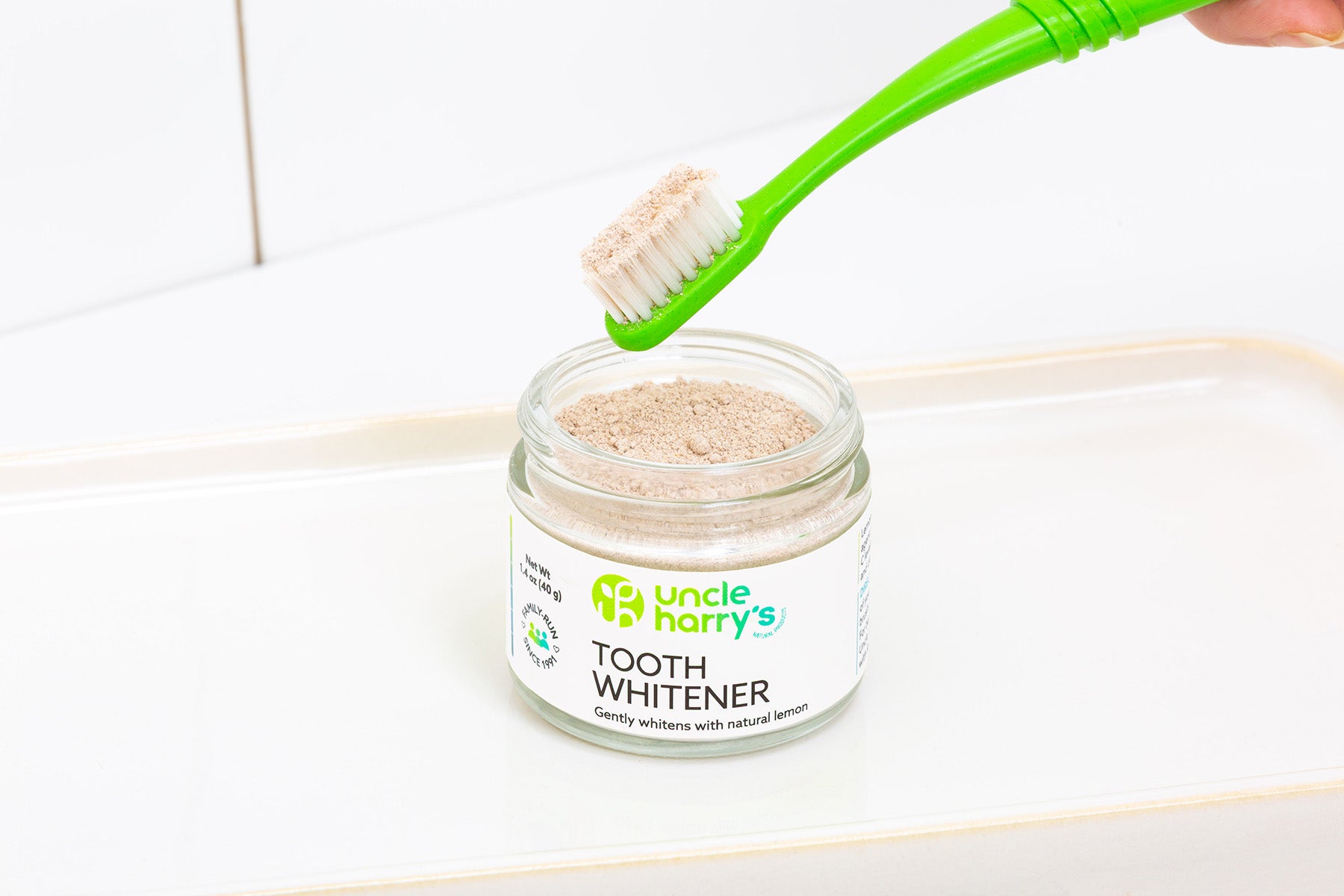 Jar of Uncle Harry's Tooth Whitener with a green toothbrush on a white background