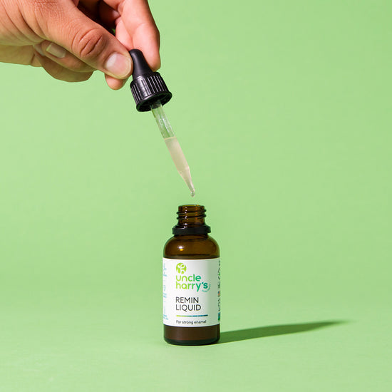 Hand using a dropper to extract liquid from an Uncle Harry's Remin Liquid bottle on a green background