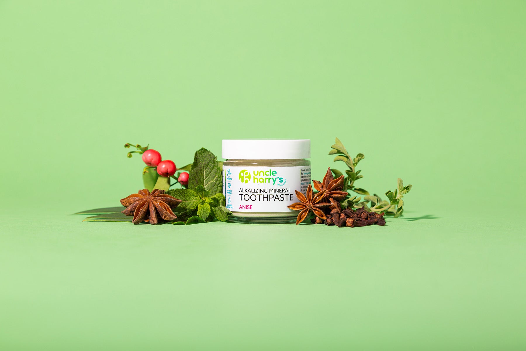 Jar of Uncle Harry's All-Natural Star Anise Toothpaste with herbs on a green background