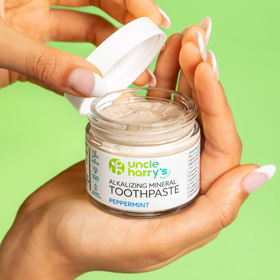 Hand holding a jar of Uncle Harry's Peppermint Alkalizing Mineral Toothpaste against a green background