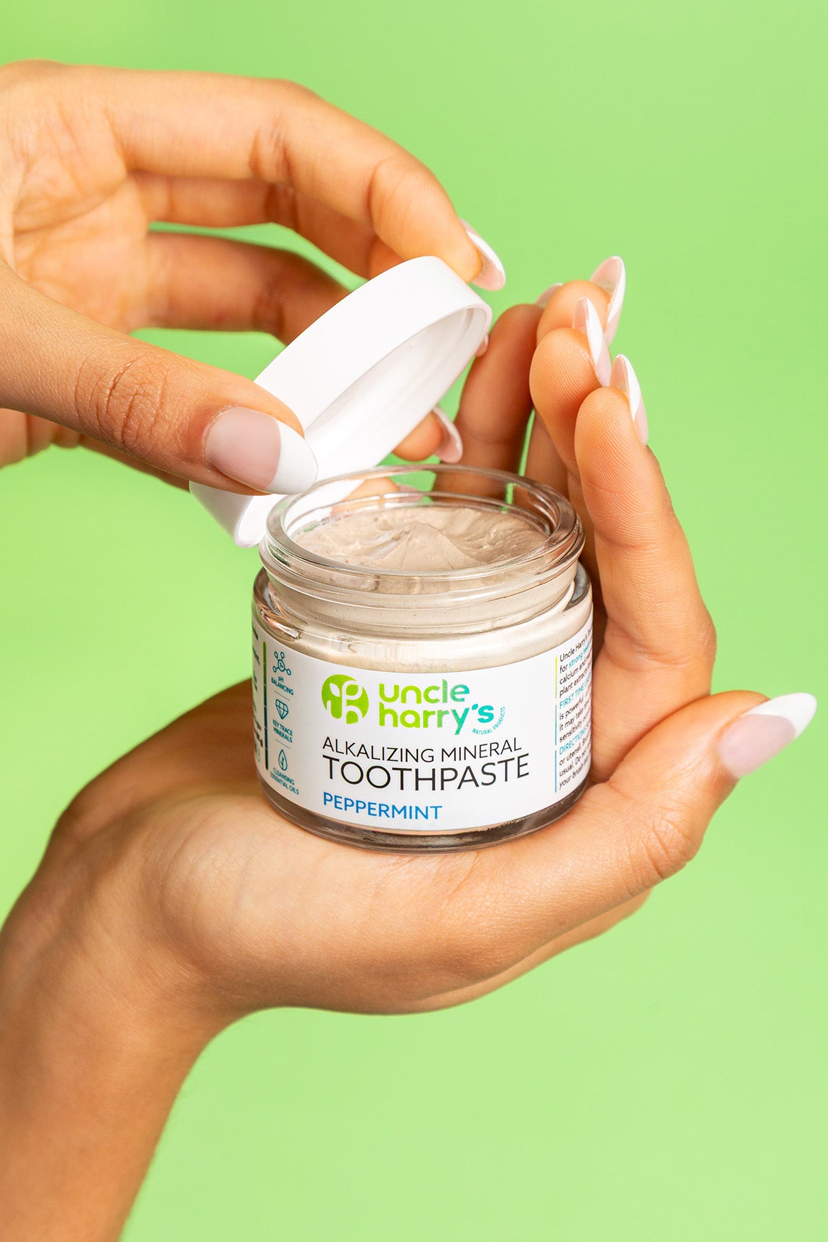 Hand holding a jar of Uncle Harry's Peppermint Alkalizing Mineral Toothpaste against a green background