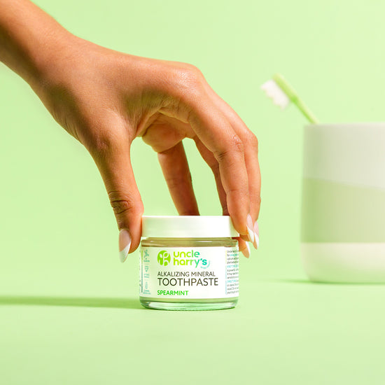 Hand holding a jar of Uncle Harry's Spearmint Toothpaste against a green background