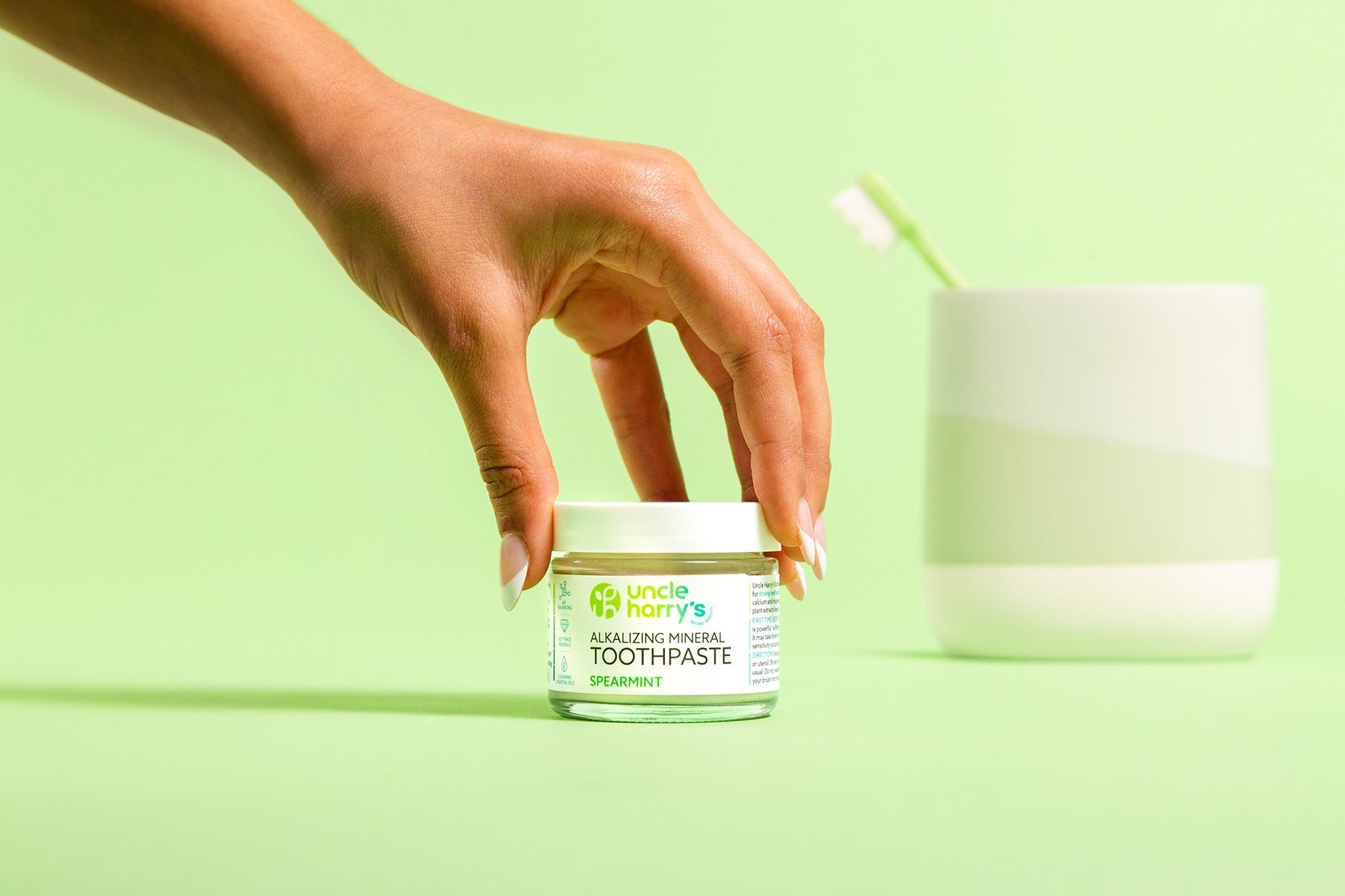 Hand holding a jar of Uncle Harry's Spearmint Toothpaste against a green background