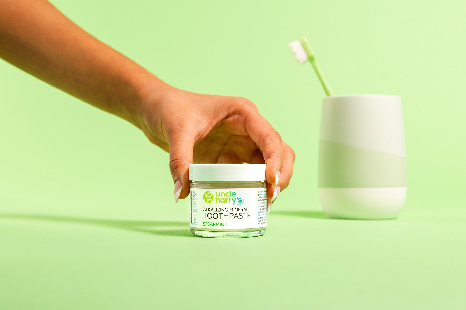 Hand holding a jar of Uncle Harry's Spearmint Toothpaste with a green background