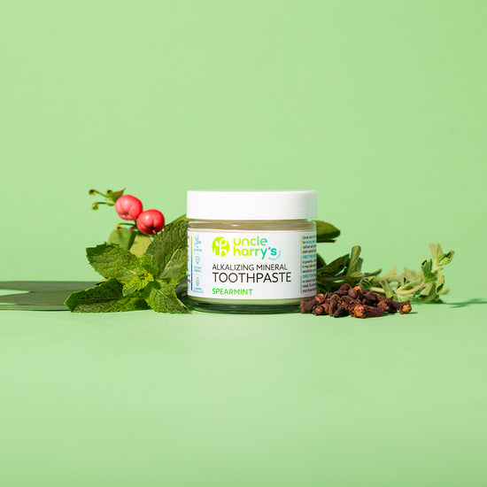 Jar of Uncle Harry's Natural Spearmint Toothpaste with mint leaves and berries on a green background