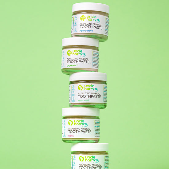 Five jars of Uncle Harry's Toothpaste stacked on a green background