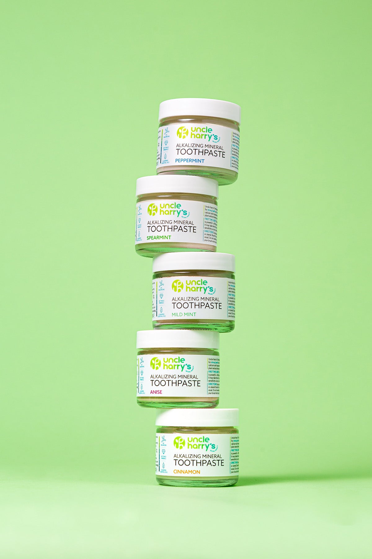 Five jars of Uncle Harry's Toothpaste stacked on a green background
